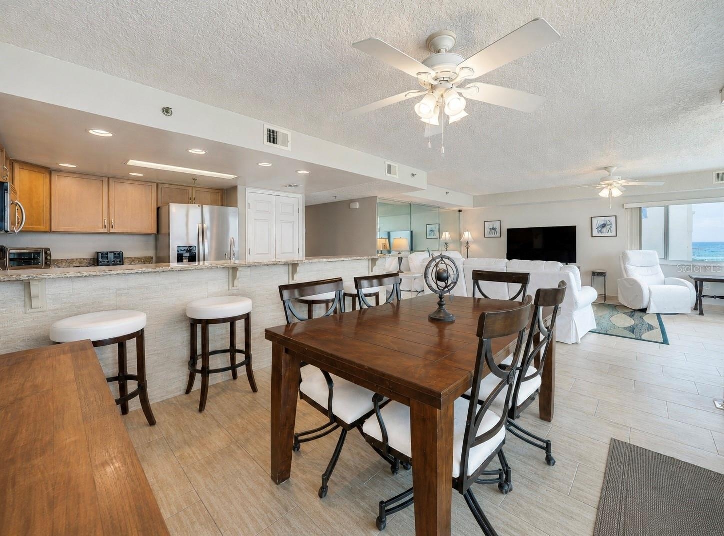 A central dining area connects to the kitchen and living space, all under ceiling fans and surrounded by windows—ideal for casual meals and gatherings