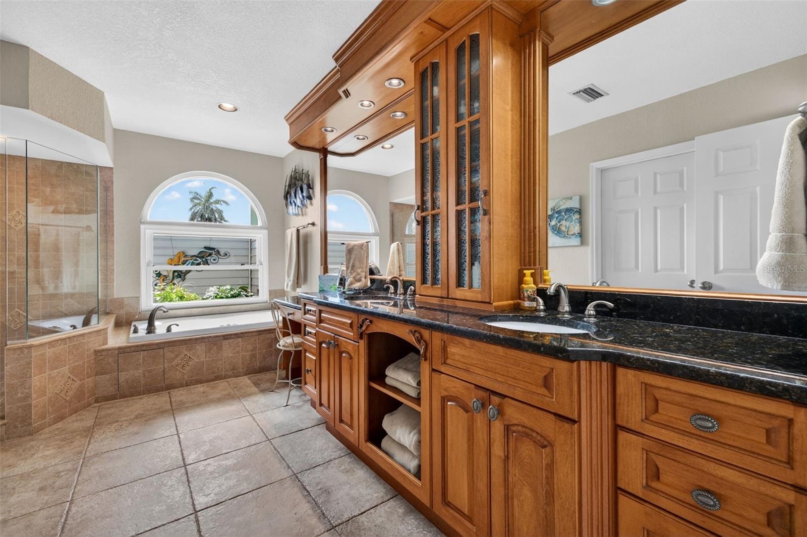 Elegant custom bath features dual sink and storage areas with built-in lighting, jetted garden tub, separate shower and walk-in closet