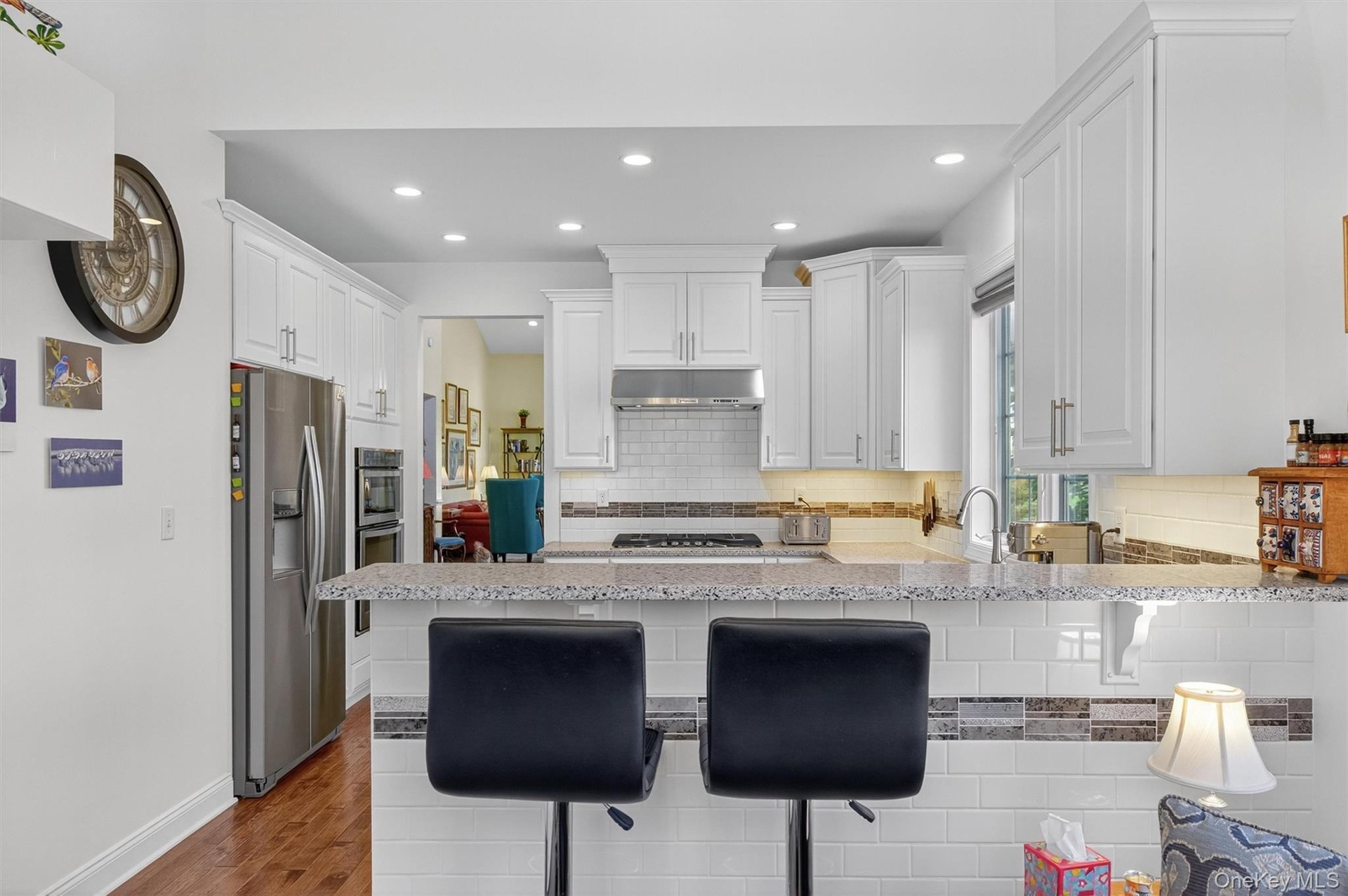Kitchen with white cabinets, a peninsula, dark wood-style flooring, appliances with stainless steel finishes, and a kitchen breakfast bar