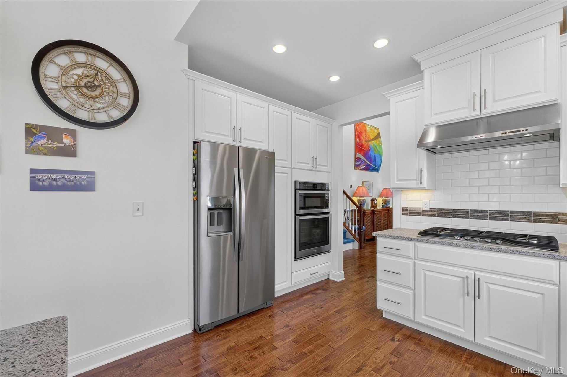 Kitchen featuring backsplash, stainless steel appliances, white cabinets, under cabinet range hood, and dark wood finished floors