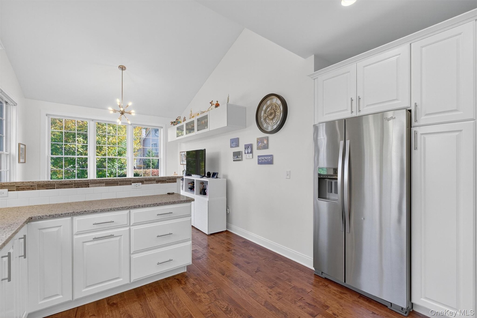 Kitchen featuring white cabinets, stainless steel refrigerator with ice dispenser, lofted ceiling, dark wood-type flooring, and light stone counters