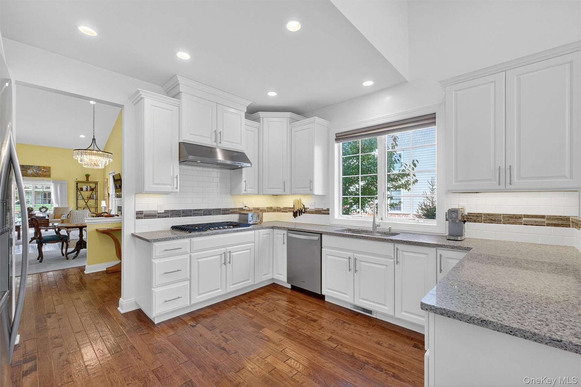 Kitchen with white cabinets, dark wood finished floors, light stone countertops, tasteful backsplash, and recessed lighting