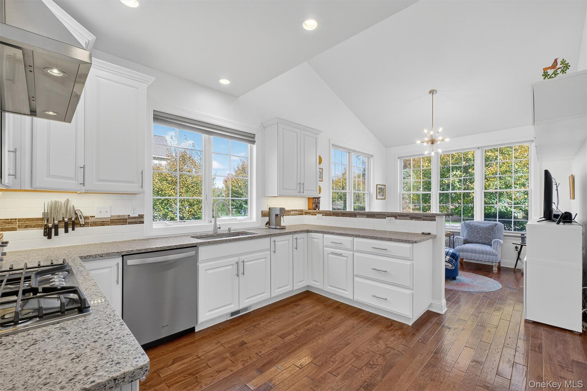 Kitchen with wall chimney exhaust hood, white cabinets, backsplash, dark wood finished floors, and lofted ceiling