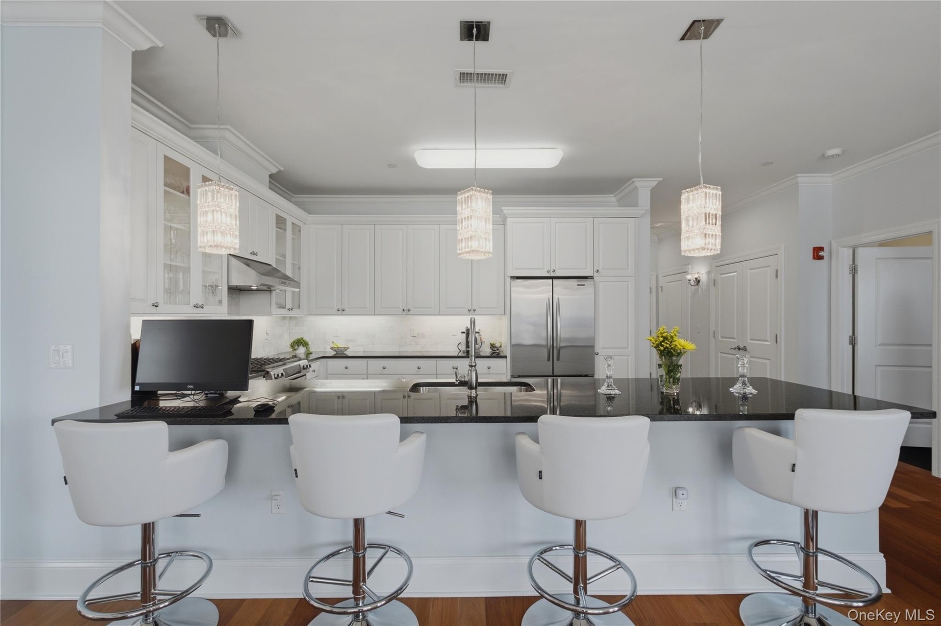 Alternate view of the kitchen, showcasing elegant pendant lighting, stainless steel appliances, and seating for four at the breakfast bar.