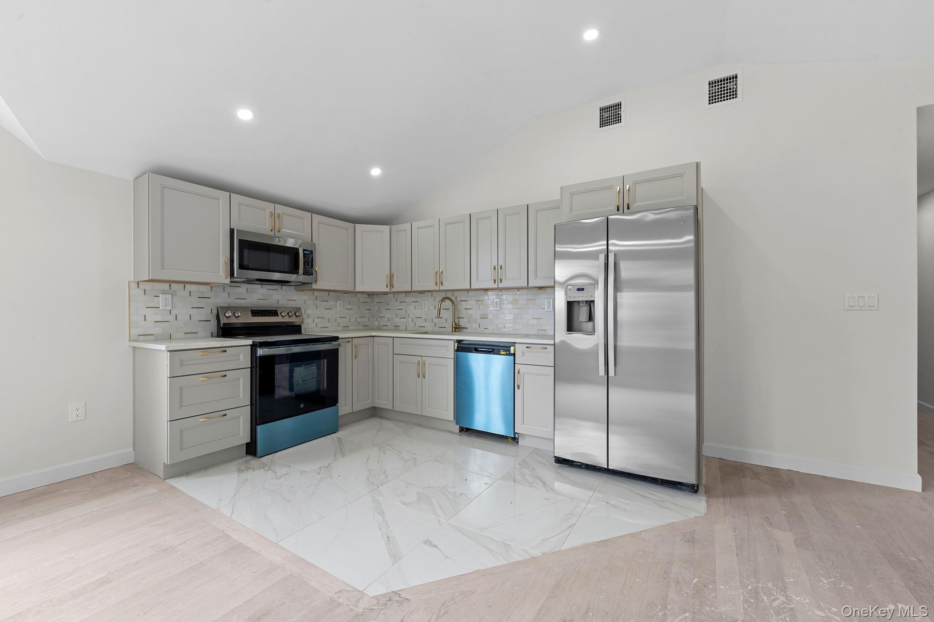 Modern kitchen featuring light gray cabinetry with gold-tone hardware, stainless steel appliances, a patterned tile backsplash, and recessed lighting