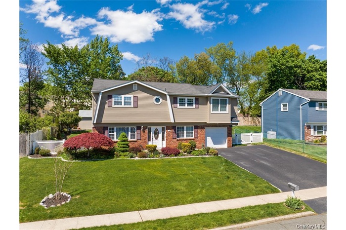 Split-level residence featuring a brick and siding facade, a manicured front lawn, a paved driveway, an attached garage, and mature landscaping