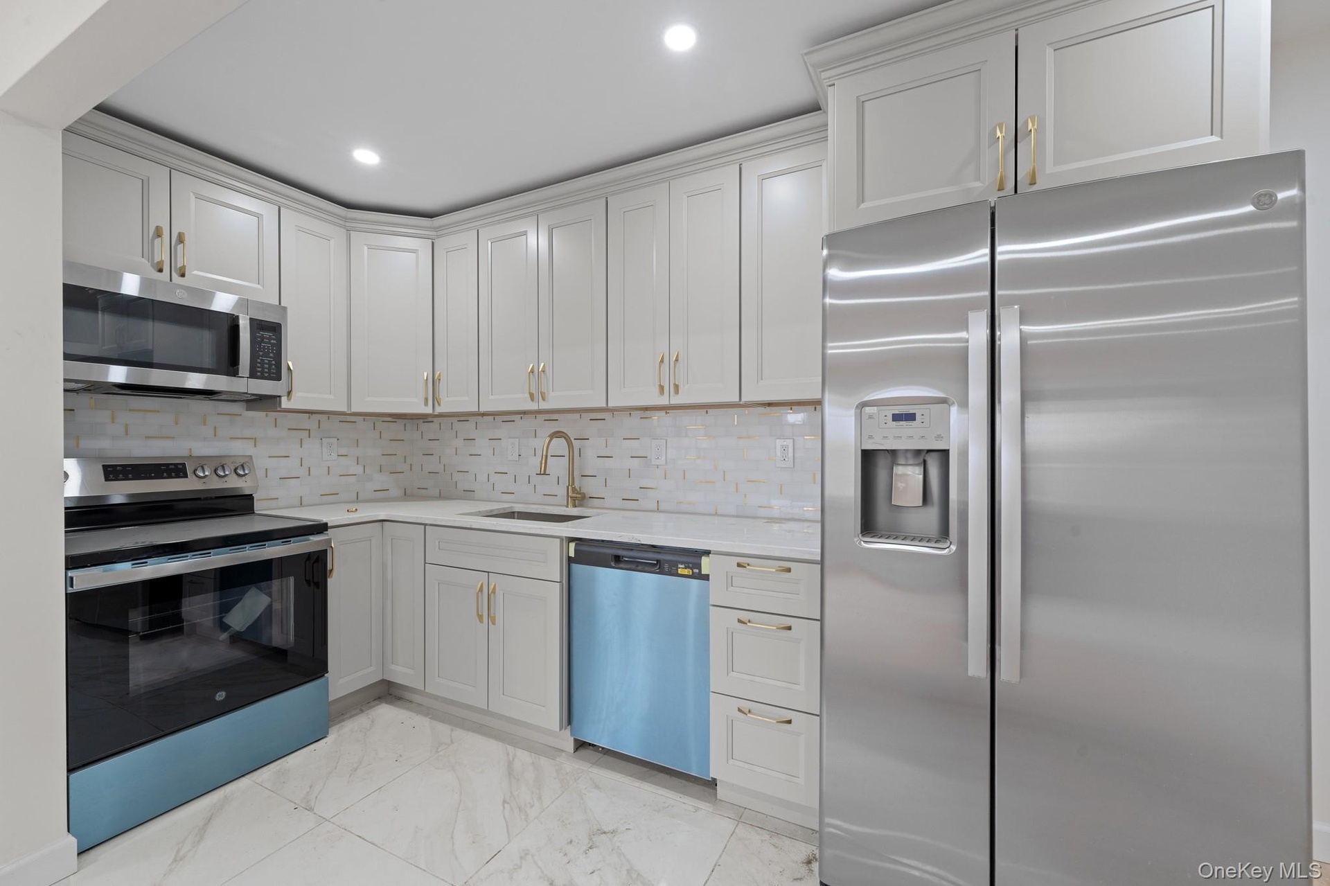 Kitchen featuring light-toned cabinetry with gold-toned hardware, stainless steel appliances, a white patterned backsplash, recessed lighting, and mar