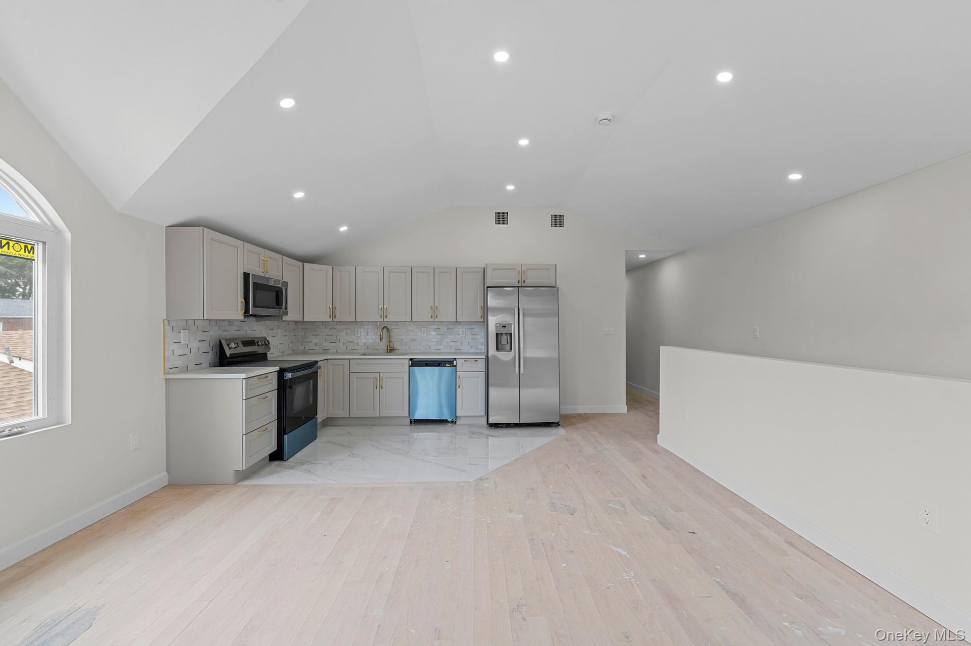Open-concept kitchen and living area featuring light wood-finish flooring, recessed lighting, and a vaulted ceiling