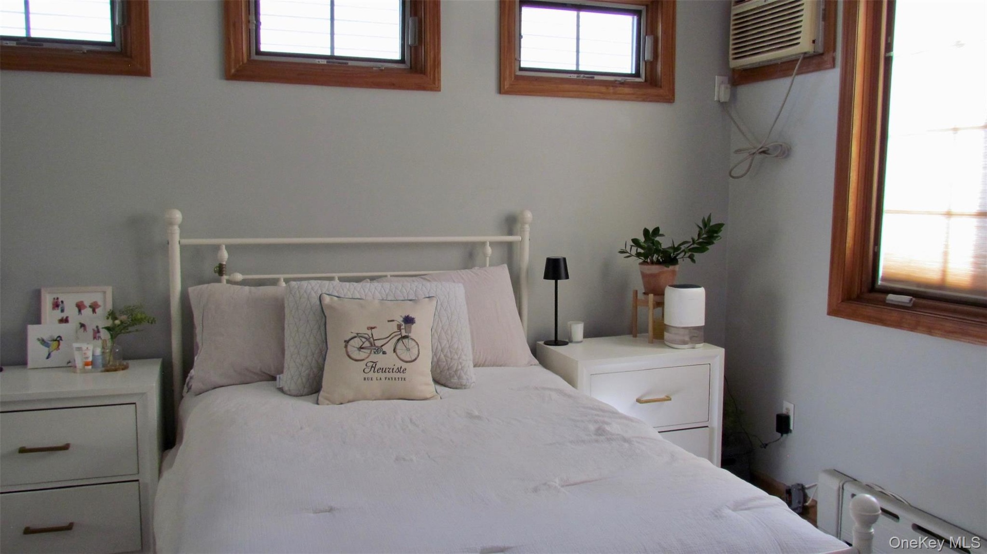 Bedroom featuring light gray walls, multiple windows with wood frames, and a built-in air conditioning unit