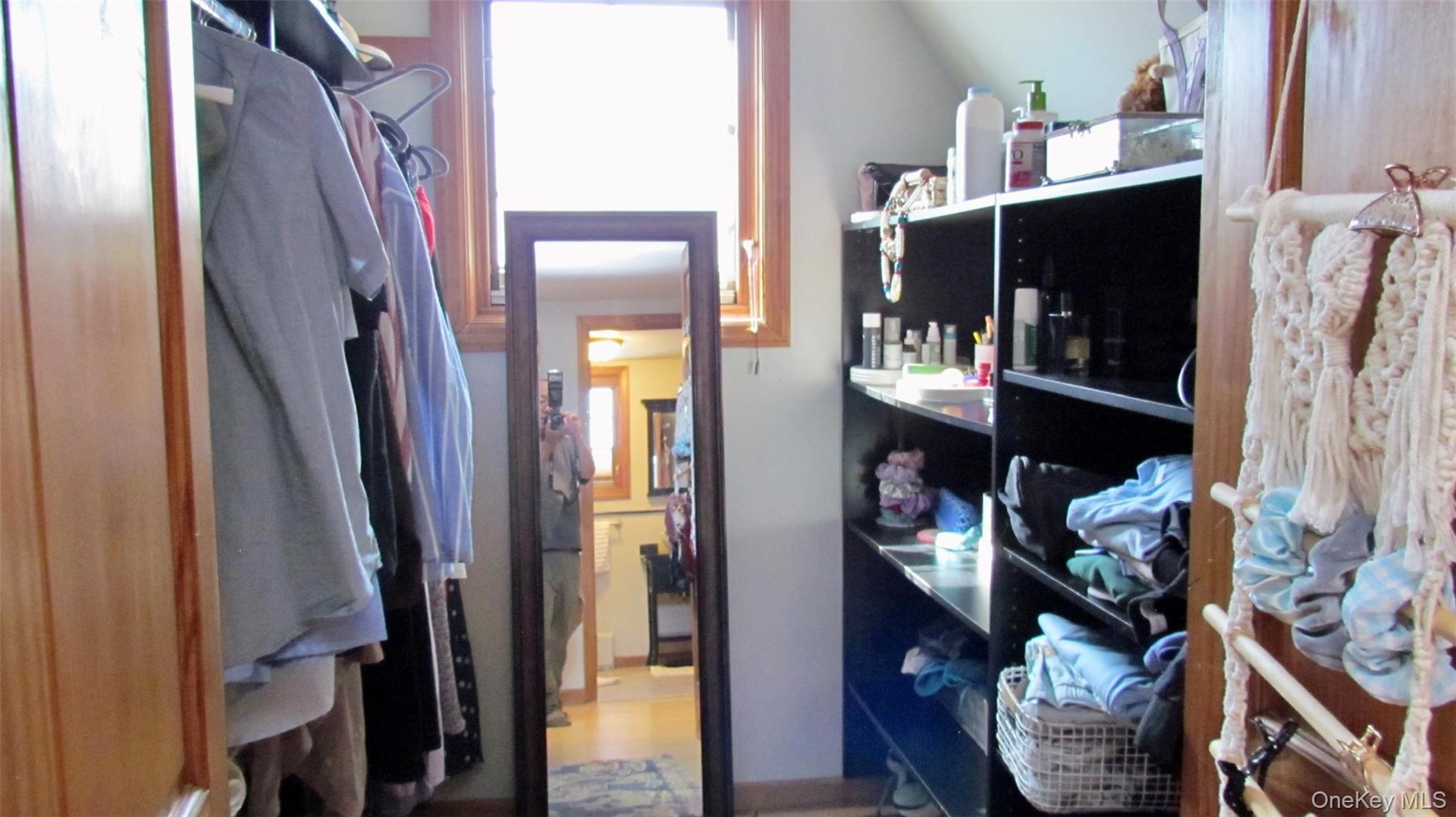 Dedicated walk-in closet space featuring a built-in shelving unit, natural wood trim around a window, and a wood-finish door frame