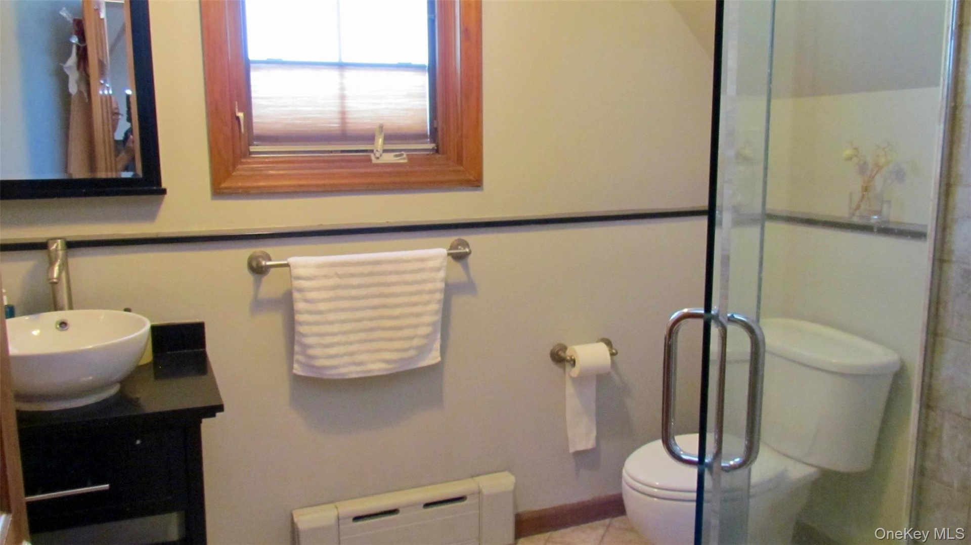 Bathroom featuring a frameless glass shower enclosure, wood-trimmed window, black vanity with vessel sink, and wall-mounted mirror
