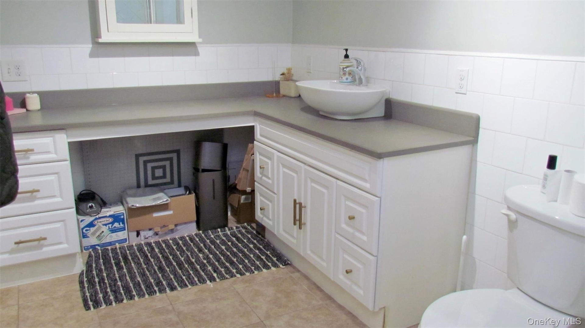 Bathroom vanity with a vessel sink, gray countertop, and white cabinetry
