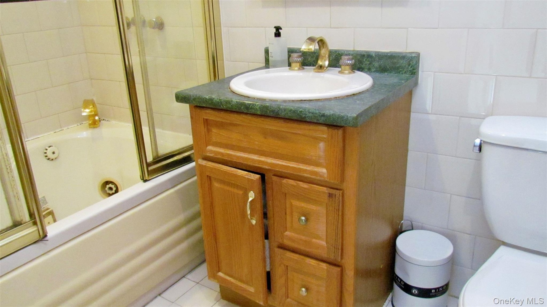 Bathroom vanity with a green countertop, integrated sink, and brass-tone fixtures