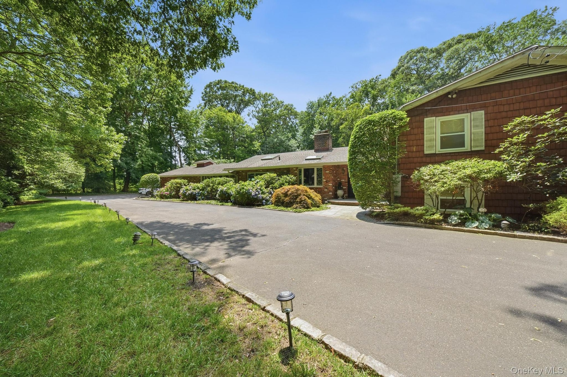 Curving asphalt driveway bordered by stone edging and landscape lighting