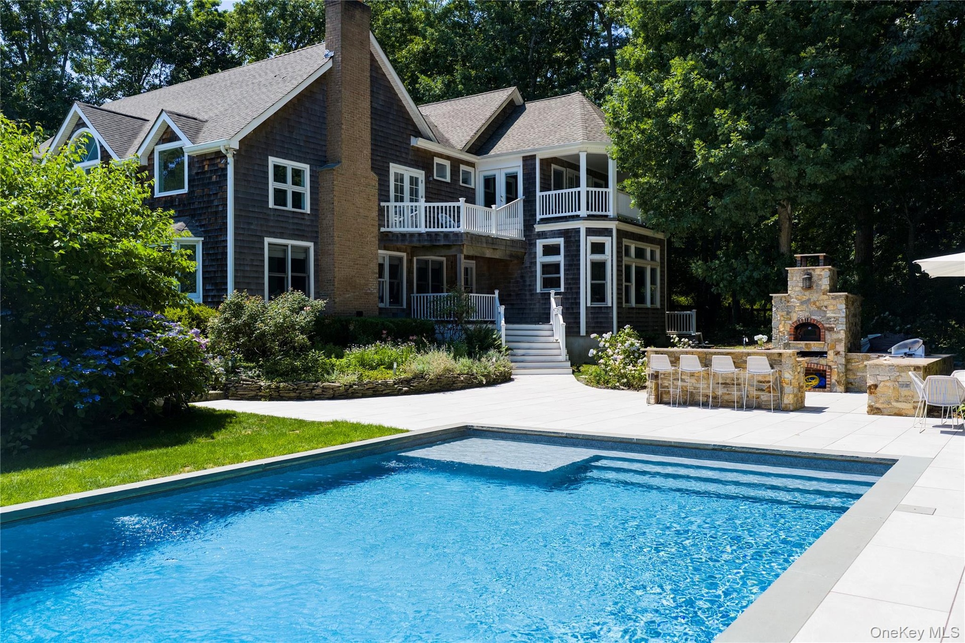 In-ground swimming pool with integrated steps and sun shelf, expansive patio, and an outdoor kitchen featuring a built-in pizza oven