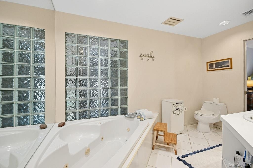 Soaking tub with jetted features, framed by a glass block wall, spa shower