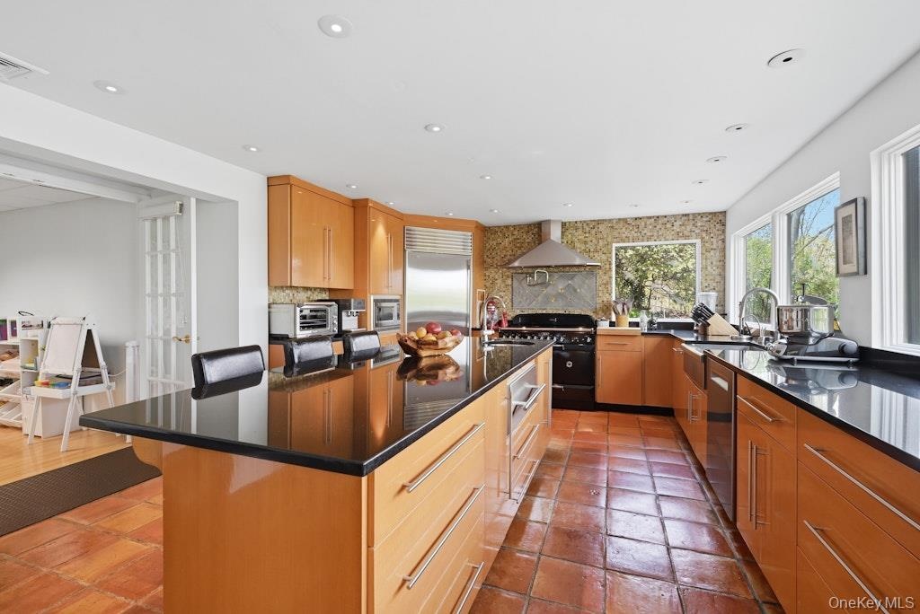 Spacious kitchen featuring an expansive island with a black countertop, natural wood-finish cabinetry, terracotta tile flooring, a large range with a 