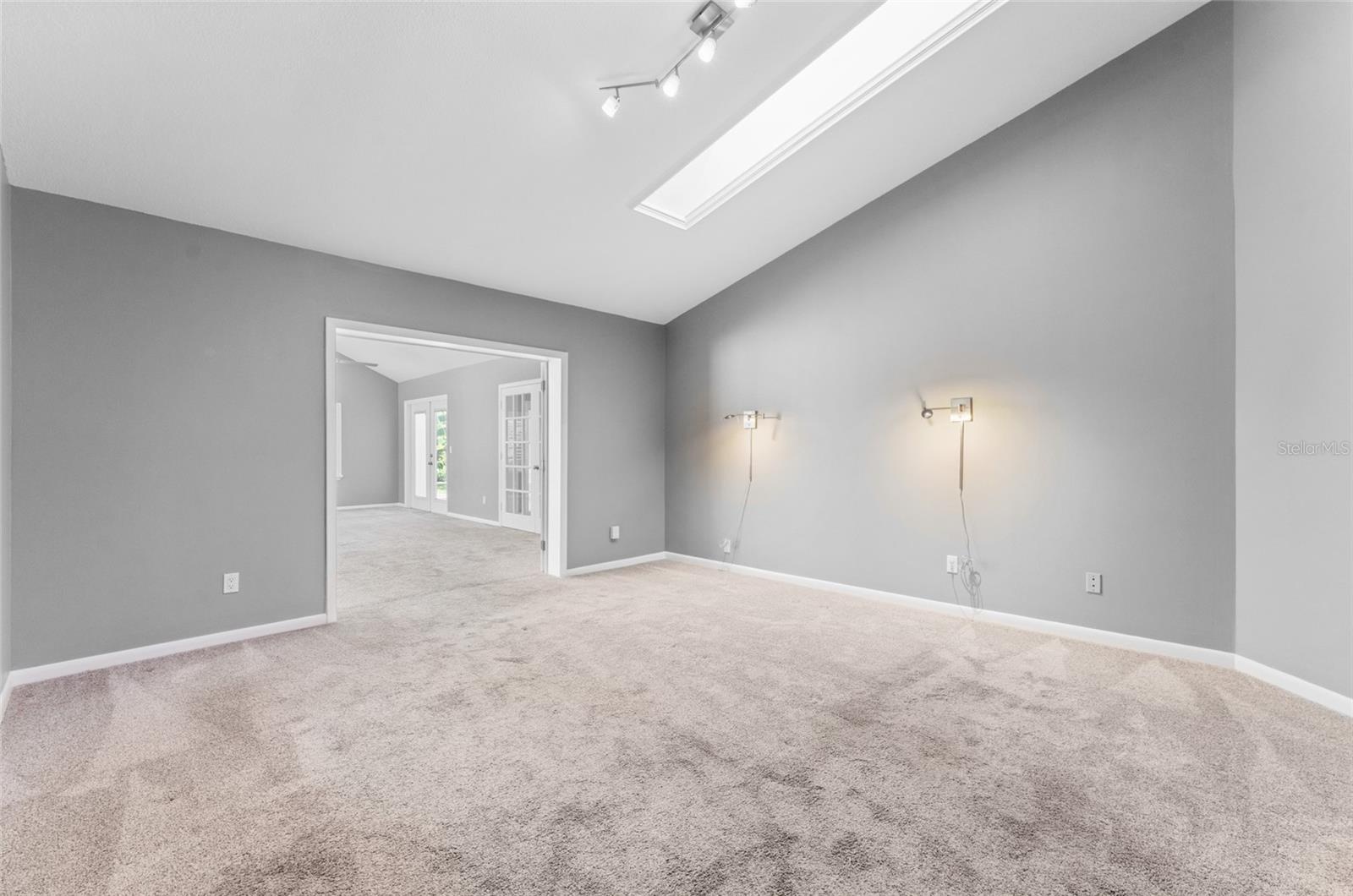 large primary bedroom looking towards bonus room with skylight and shade