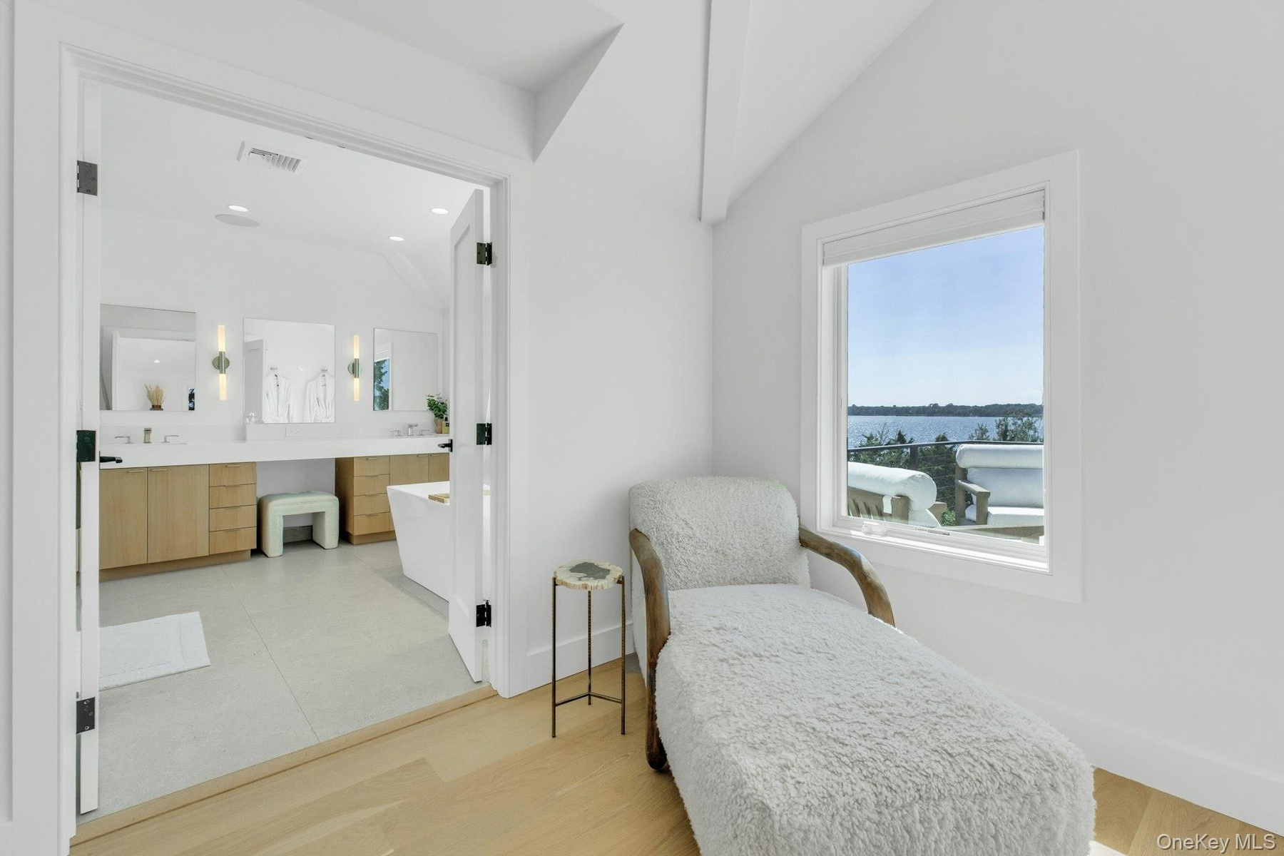 Bright interior space with light wood-finish flooring, white walls, and a window framing a water scene
