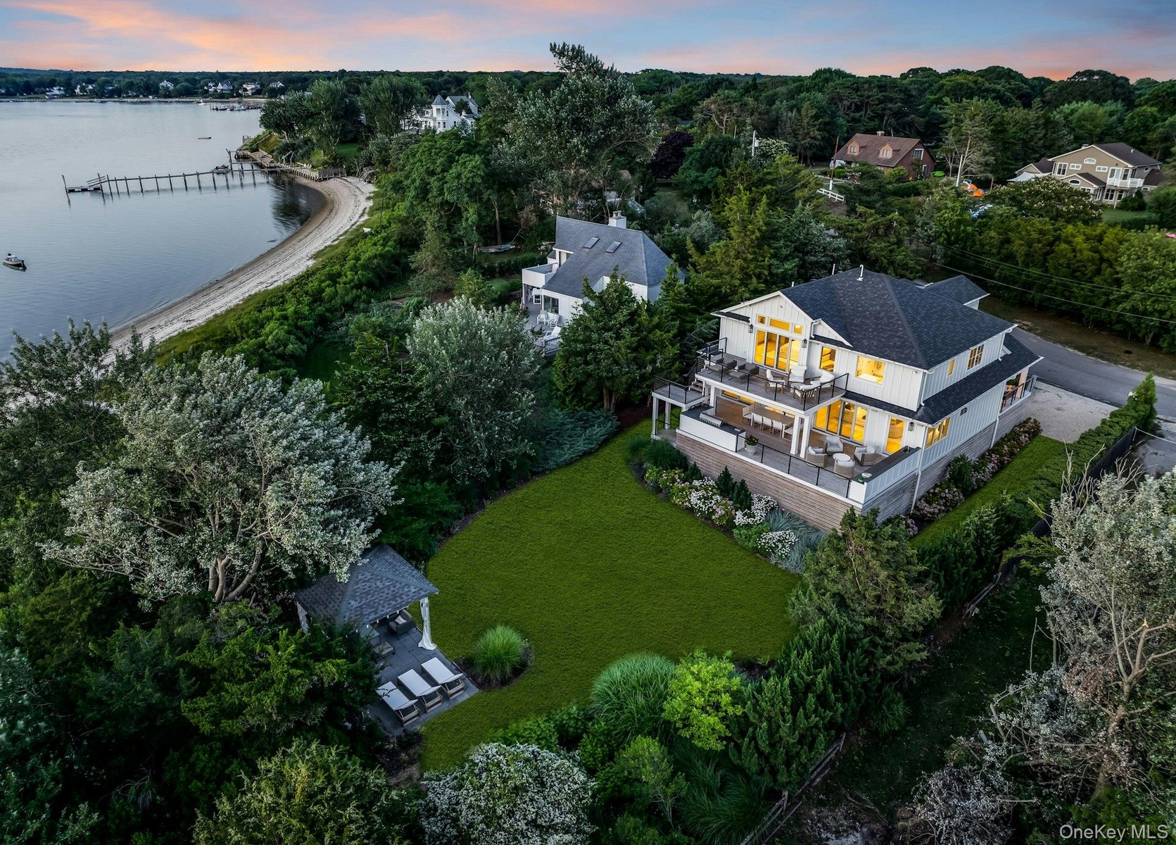 Waterfront residence featuring multiple expansive outdoor decks, a large manicured lawn, a detached gazebo, and a private beach with a dock