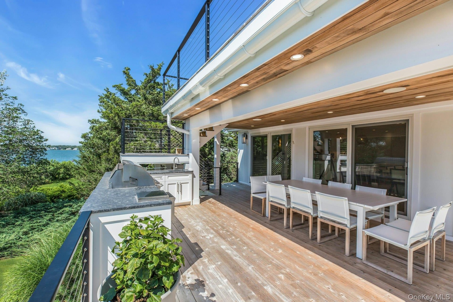 Expansive outdoor deck featuring wood-finish flooring, a built-in outdoor kitchen with grill and sink, and a cable railing system