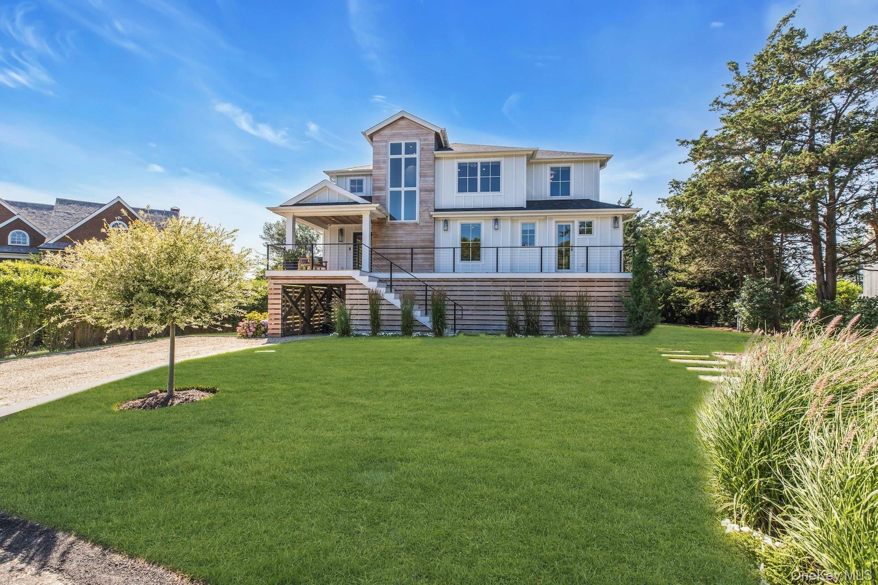 Custom coastal residence featuring board and batten siding, natural wood shingle accents, multiple balconies with black railings, and an expansive fro