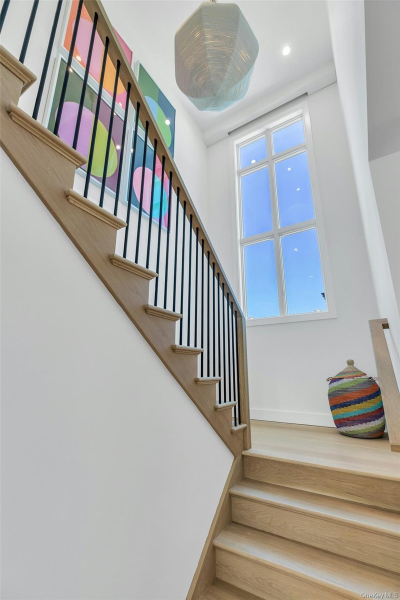 Hardwood staircase with black metal balusters and a wood-finish handrail, complemented by a tall, multi-pane window and a contemporary pendant light f