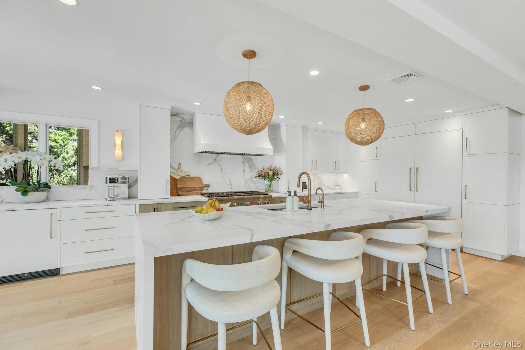 Spacious kitchen featuring an oversized island with countertop seating, light wood-finish flooring, white cabinetry with gold-tone hardware, and integ