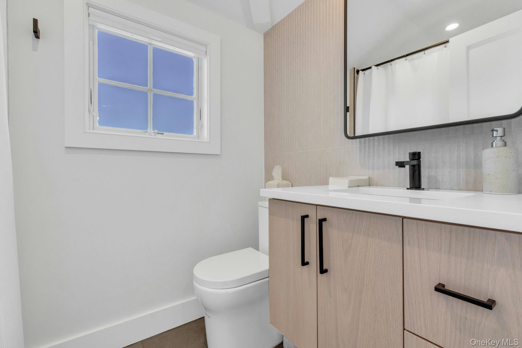 Modern bathroom featuring a wood-finish vanity with matte black hardware, white countertop, rectangular undermount sink, and a black-framed mirror