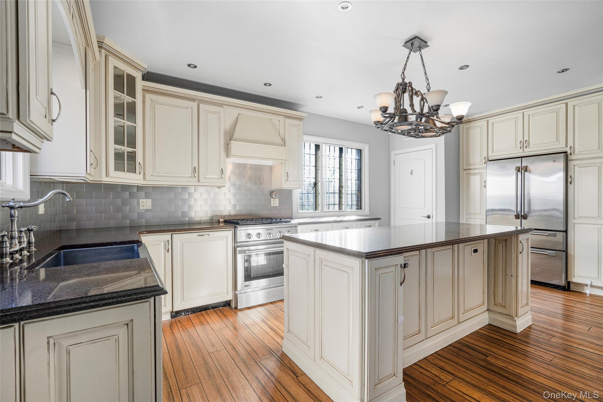 Kitchen with cream cabinetry, a center island, custom range hood, high end appliances, and sink