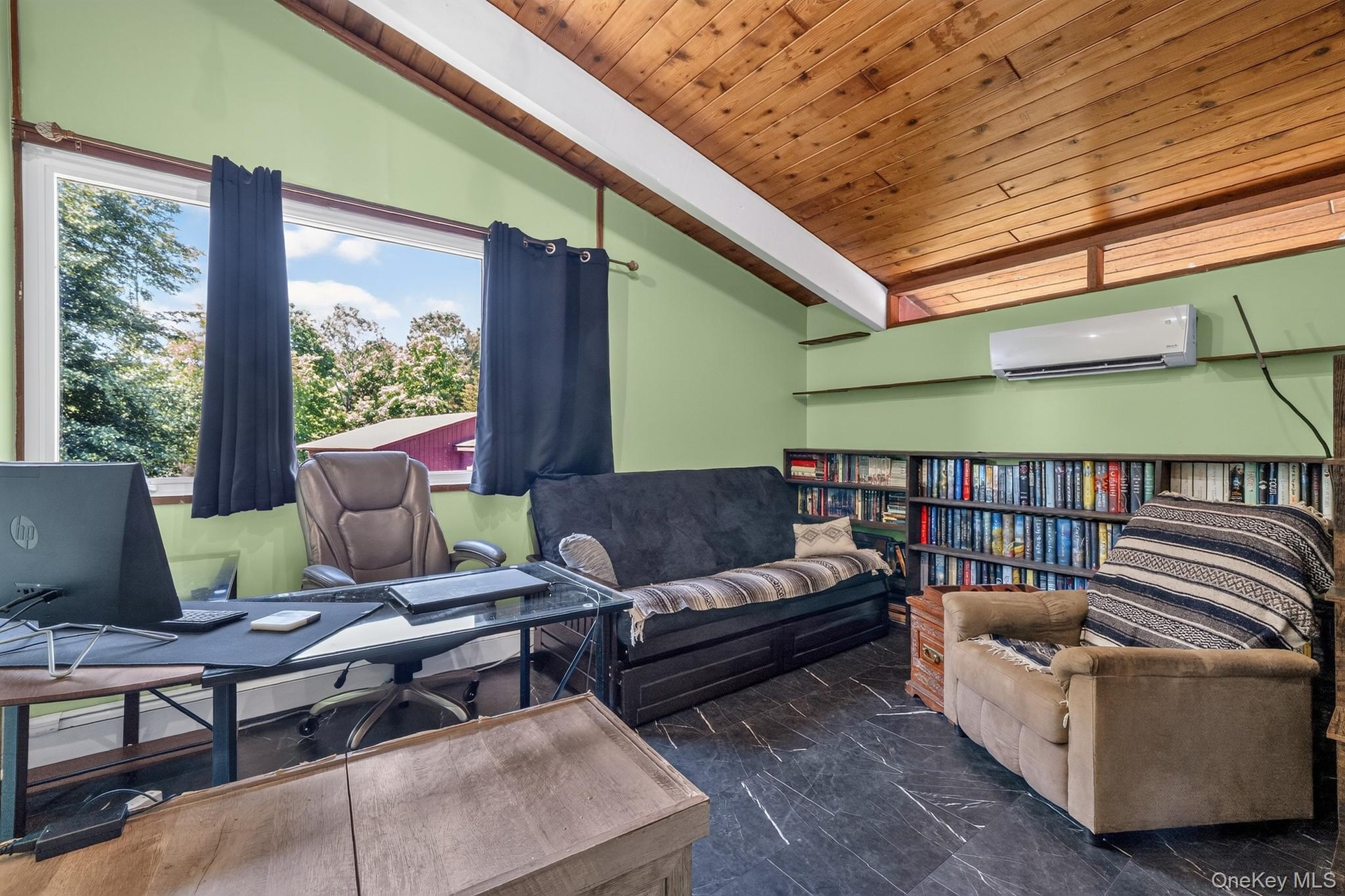 Vaulted wood-paneled ceiling with exposed beams, large picture window with outdoor scenery, full-wall built-in shelving, slate-look flooring, and a wa