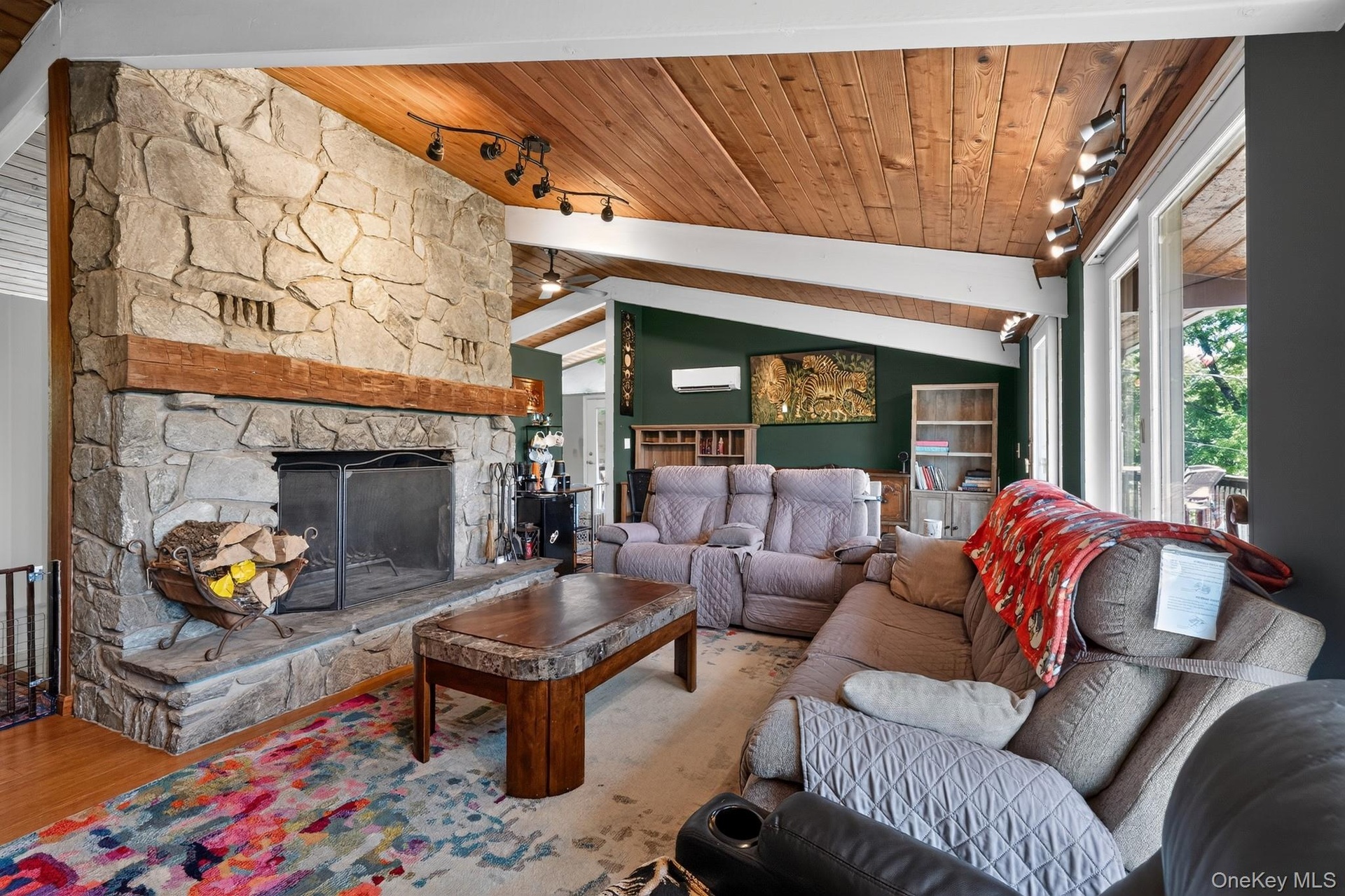Great room featuring a full-height natural stone fireplace, exposed beam wood-finish ceiling, track lighting, and a ductless mini-split system
