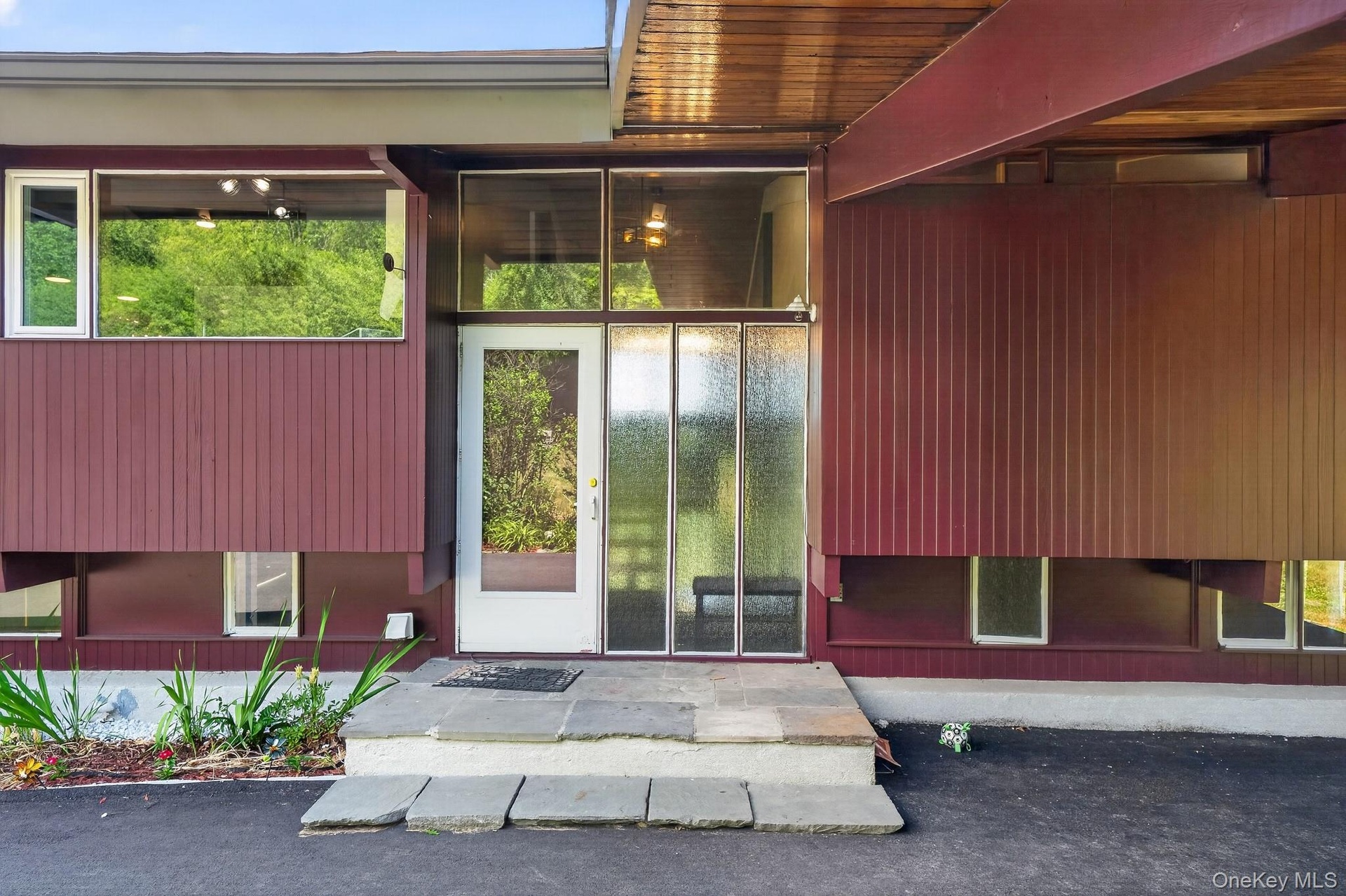 Modern exterior with rich maroon siding, prominent glass entry, and multiple large windows