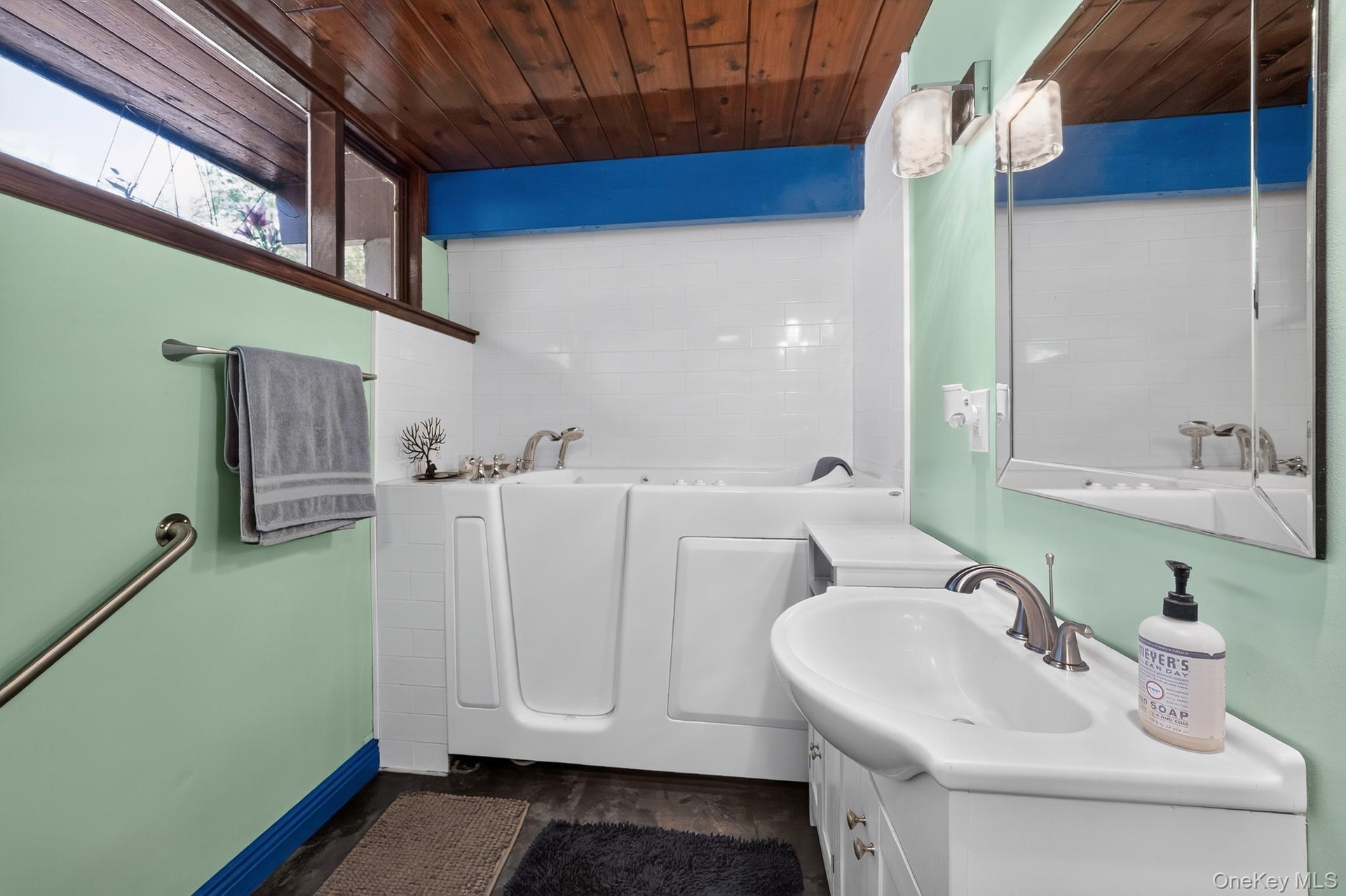 Bathroom featuring a walk-in tub, white subway tile surround, wood-finish ceiling, and an integrated vanity sink with storage