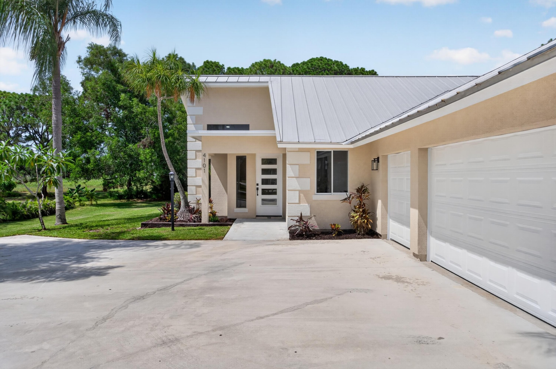 Contemporary stucco exterior with a metal roof, two-car garage, and a modern entry door featuring frosted glass panels