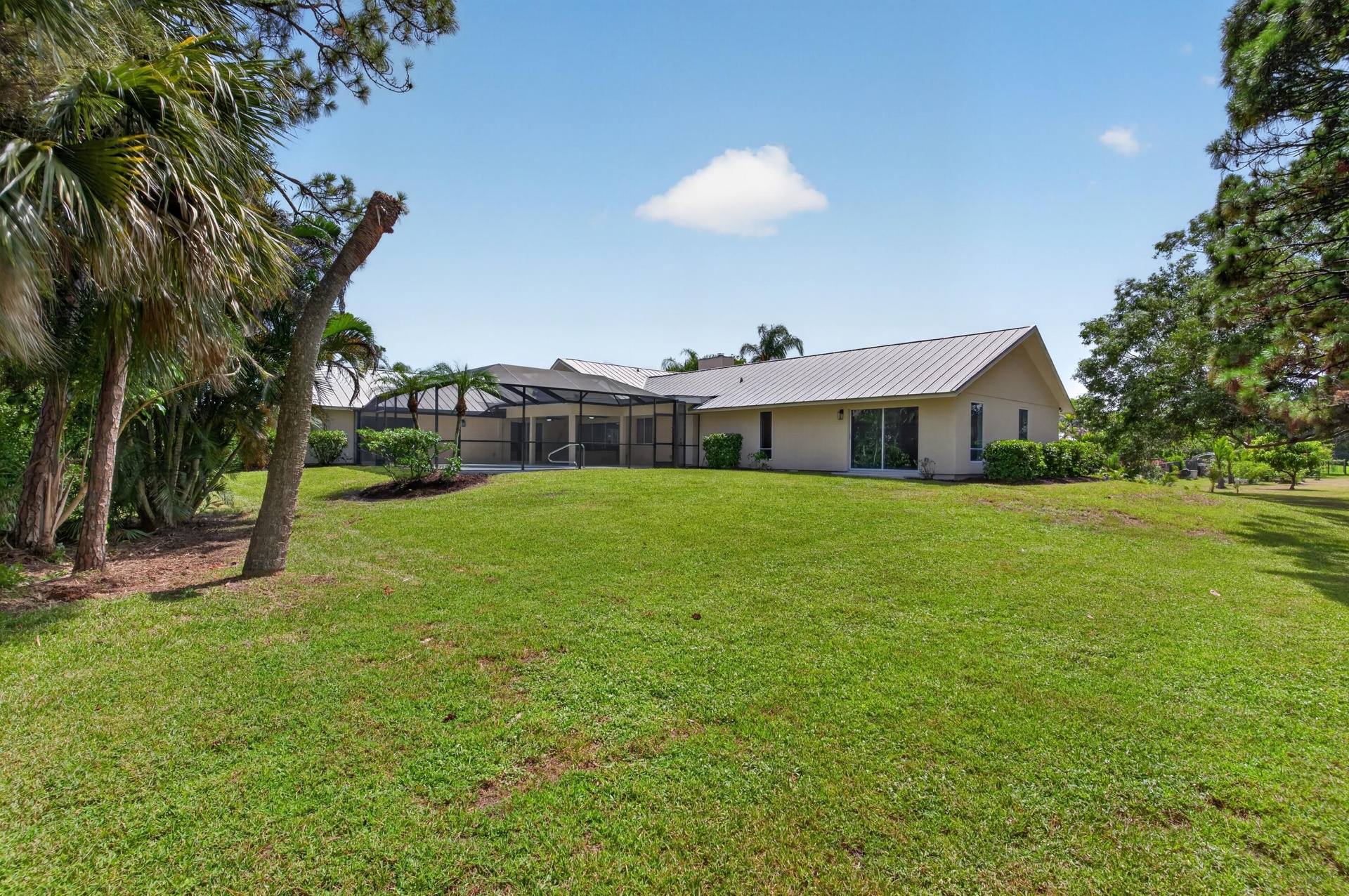 Rear exterior featuring a metal roof, screened lanai, sliding glass doors, and mature landscaping