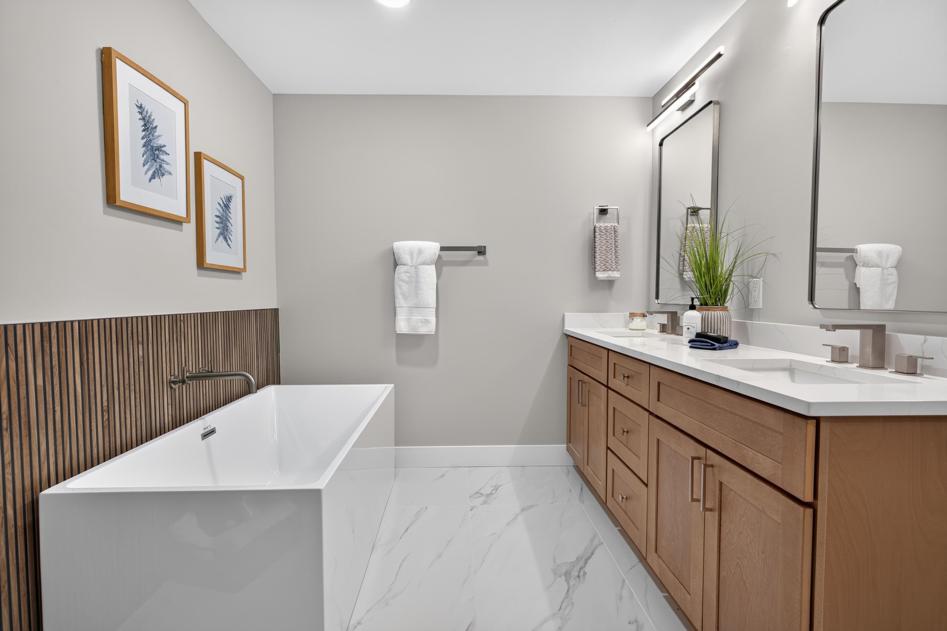 Contemporary bathroom featuring a freestanding soaking tub with wall-mounted faucet, dual vanity with undermount sinks, white countertops, and wood-fi