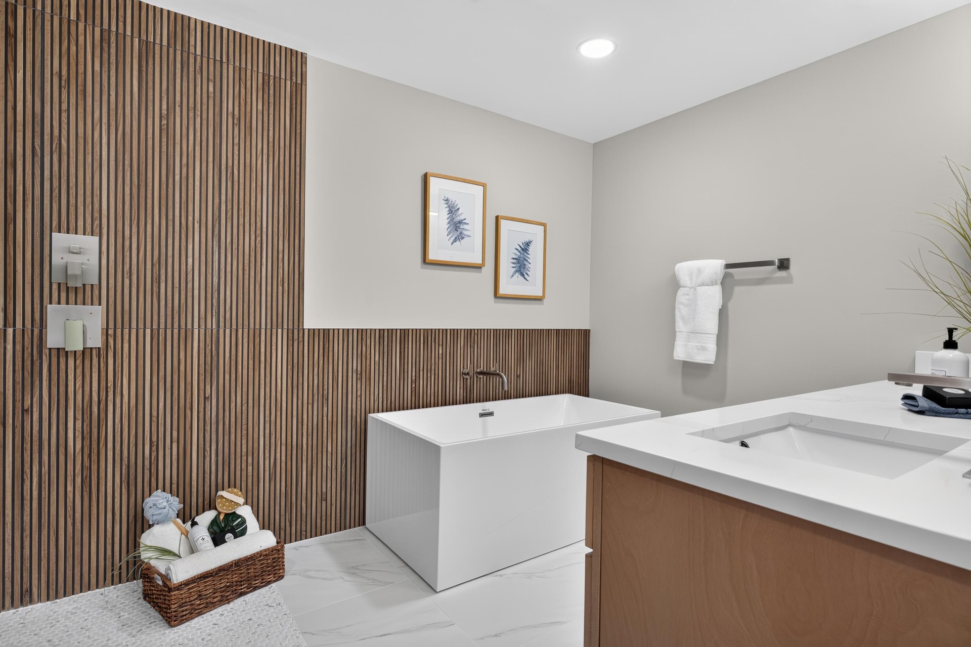 Contemporary bathroom featuring a freestanding soaking tub with wall-mounted plumbing fixtures, a wood-finish accent wall, a dual-sink vanity with an 