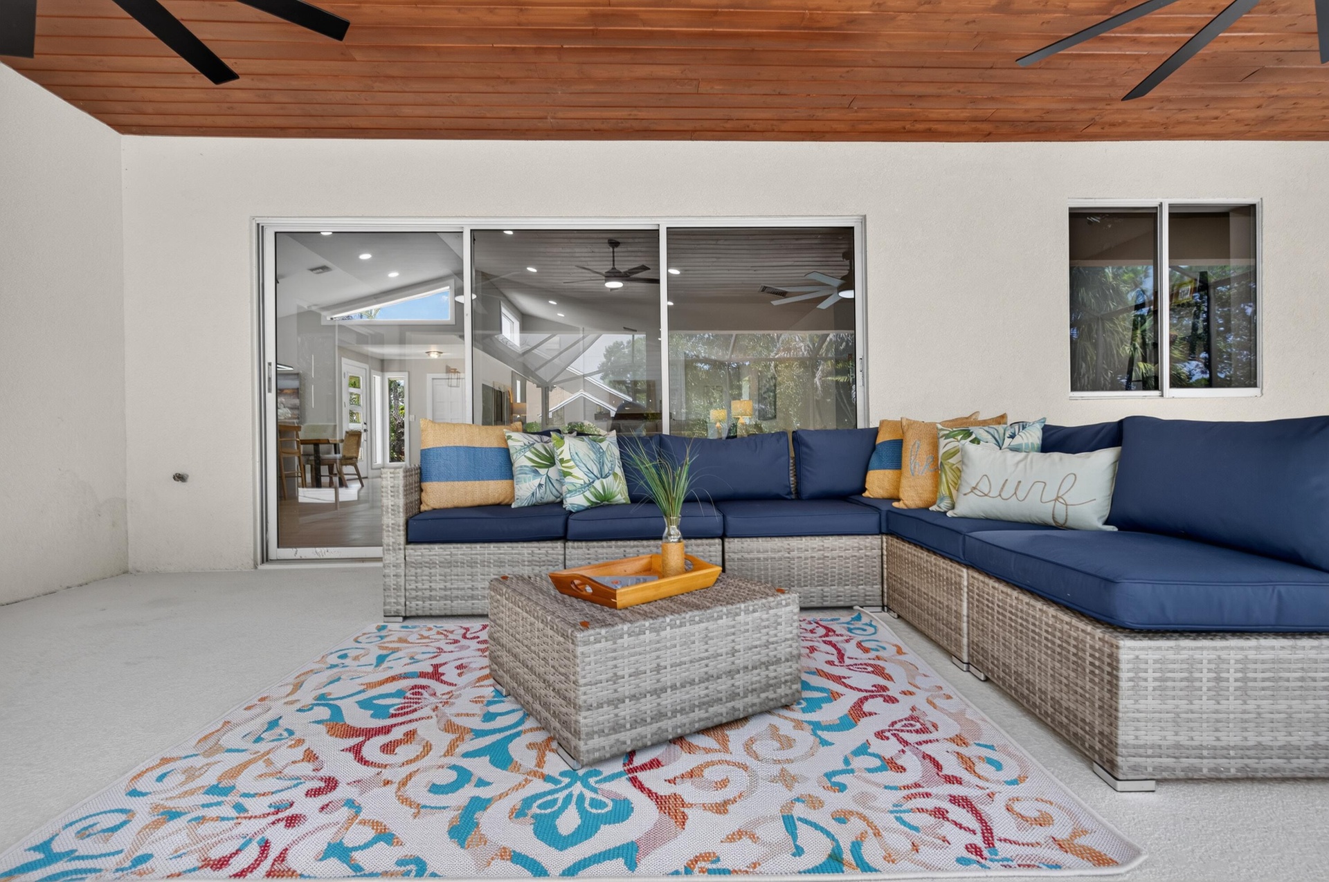 Covered patio with a wood-finish ceiling, featuring sliding glass doors, a window, and a ceiling fan
