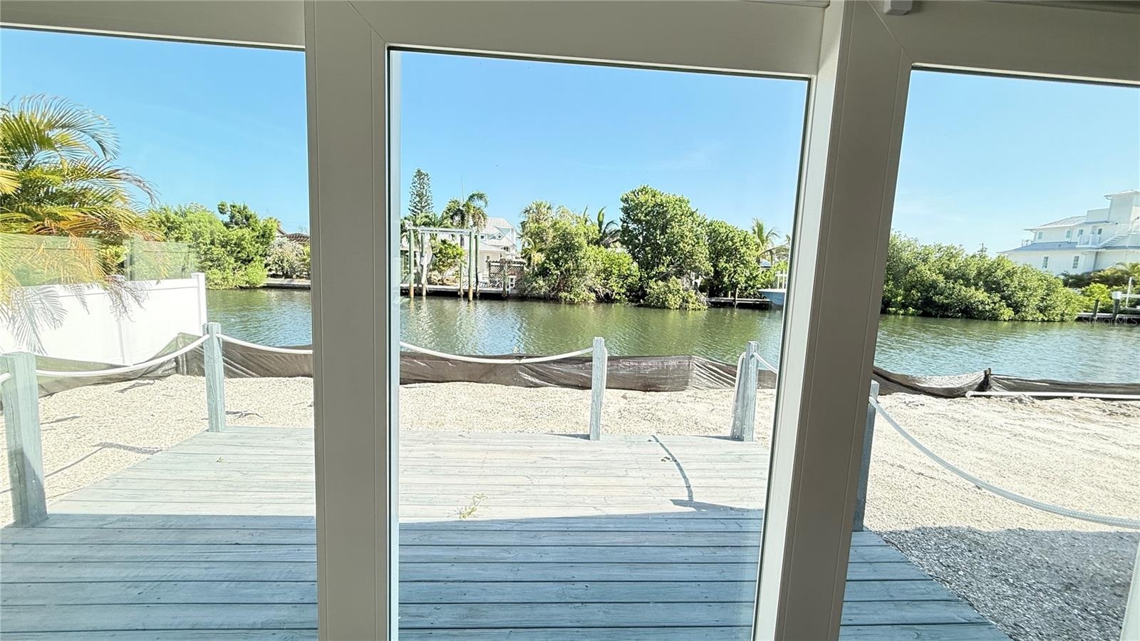 View through sliding door of deck and canal.  Black tarp at seawall is for adjacent unit new pool install.