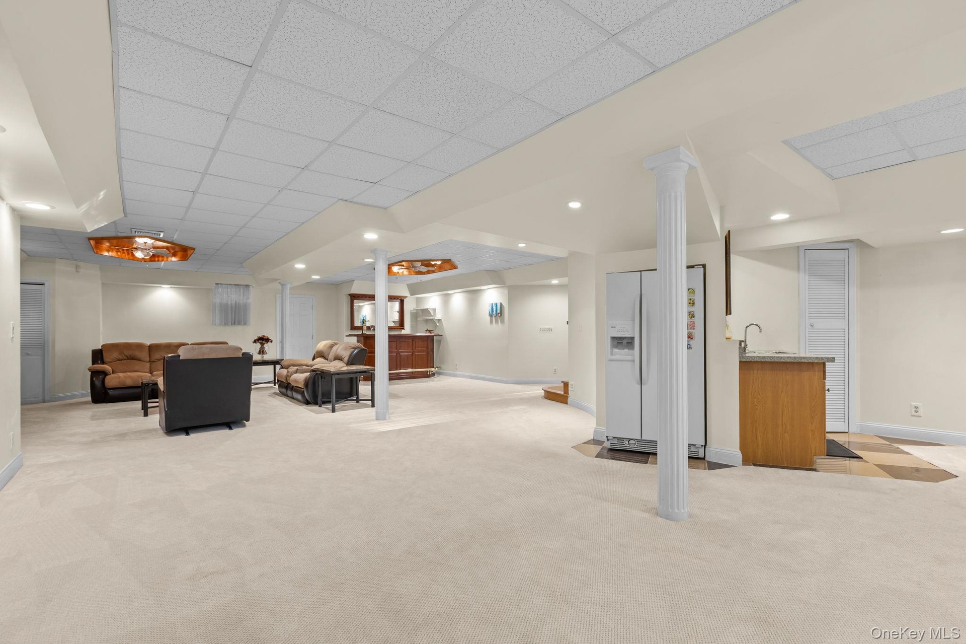 Designed for effortless entertaining, this expansive recreation space features a refrigerator, cabinetry with sink, and high ceilings, creating a vers
