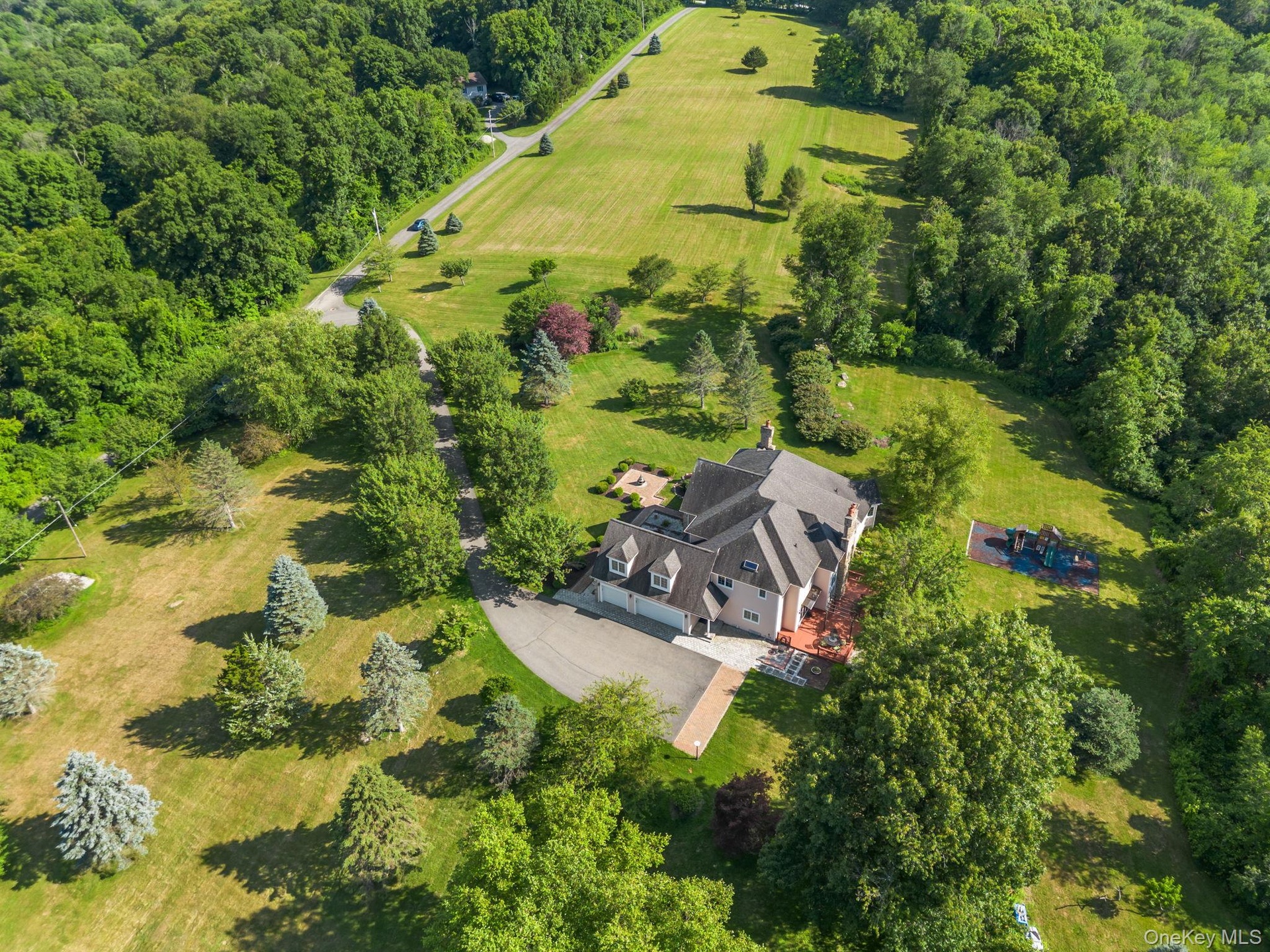 A stunning aerial perspective reveals the harmony of this country estate’s expansive grounds, lush landscaping, open spaces, and wooded backdrop.