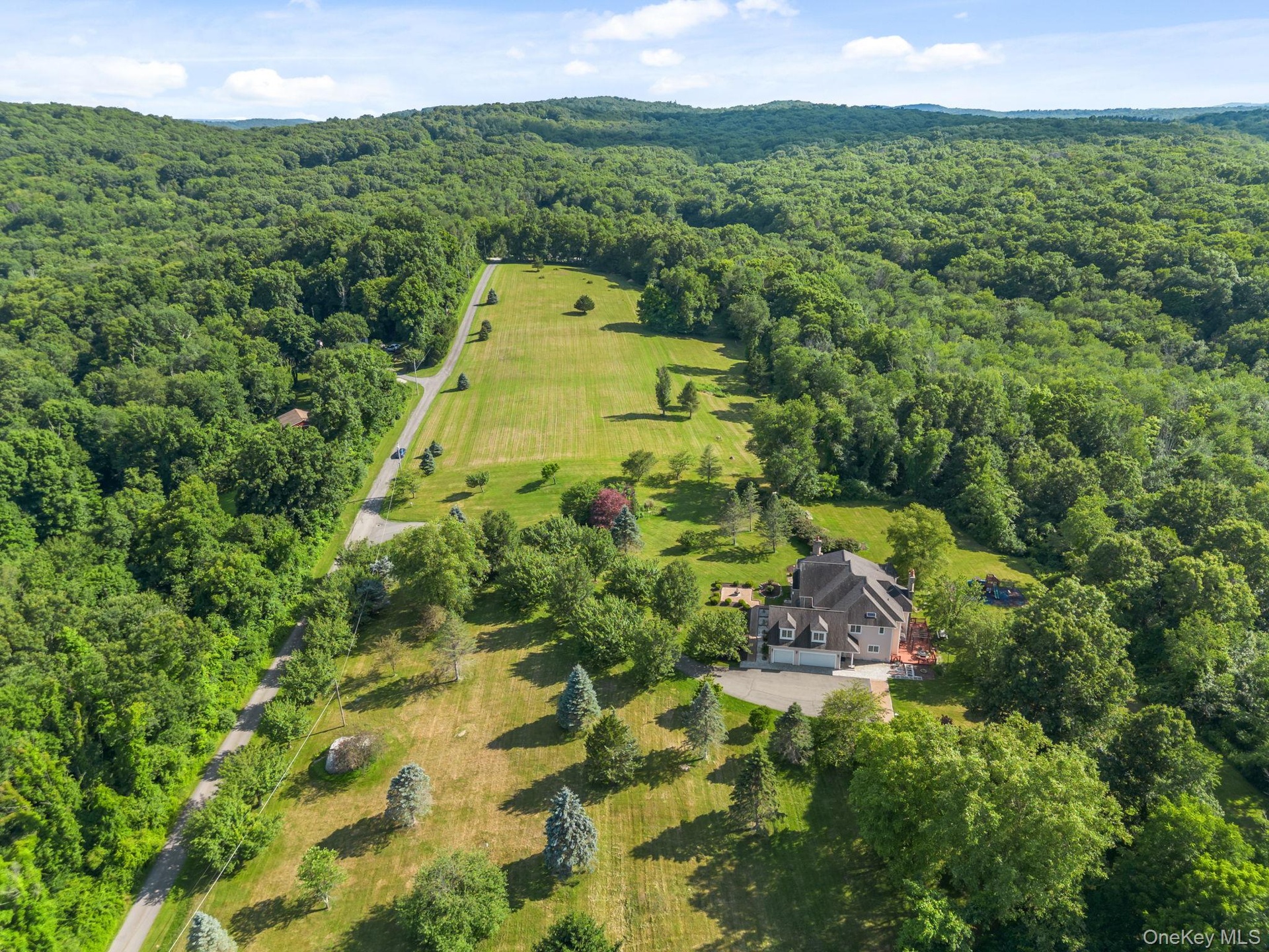 A breathtaking aerial perspective reveals the property’s pristine acreage, beautifully maintained landscaping, open level lawns, and mature wooded are