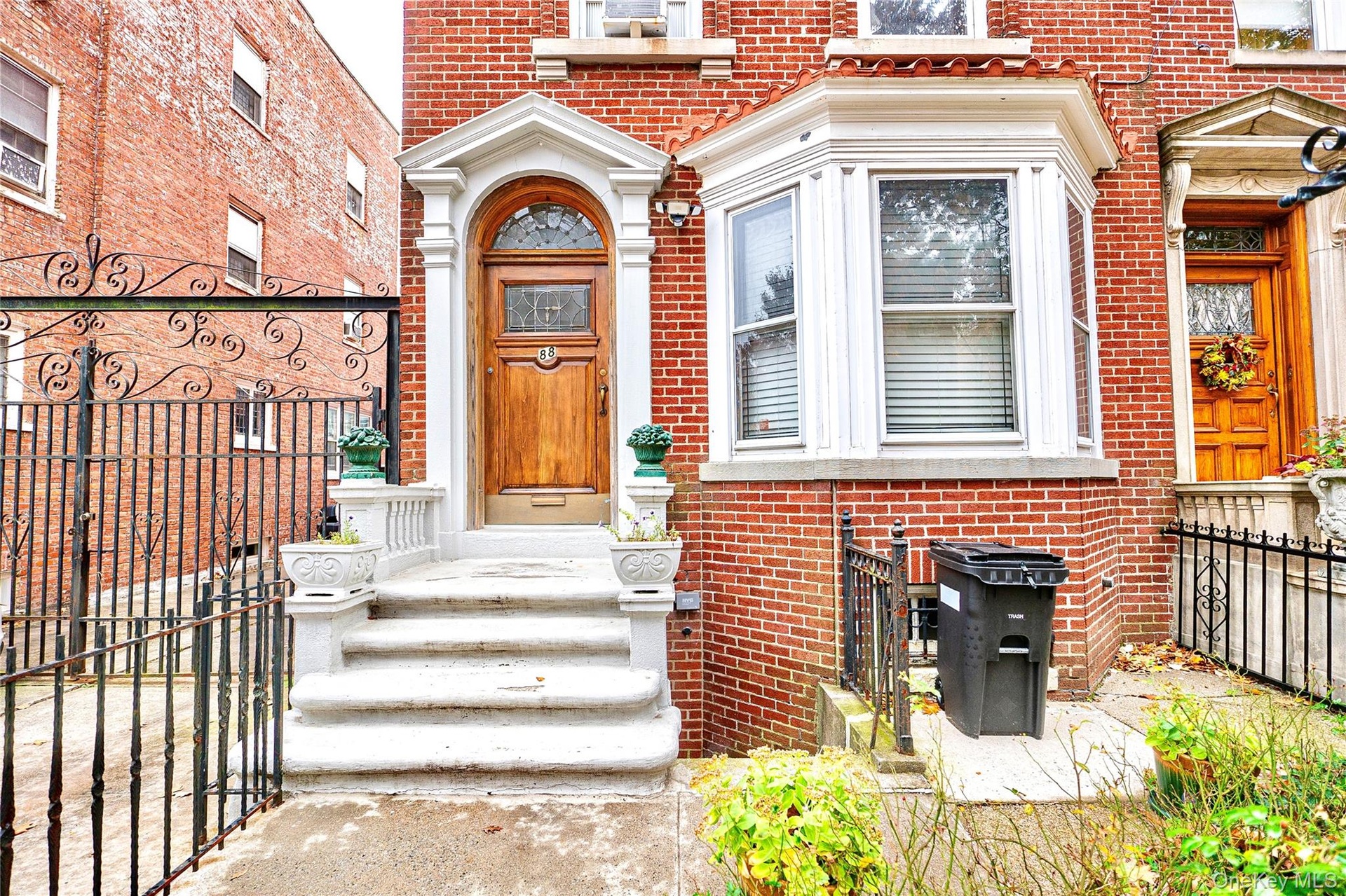 Brick facade with a bay window and arched wooden entry door featuring decorative glass