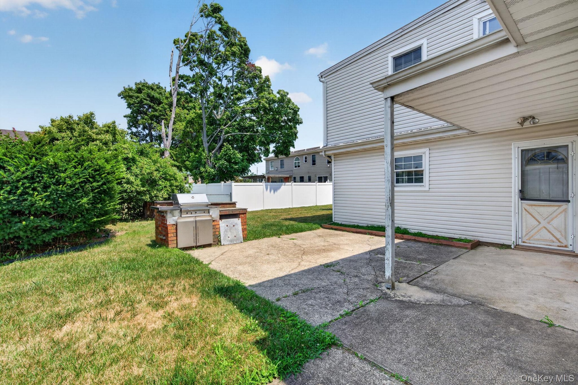 Rear exterior featuring a covered patio area with a concrete surface, white vinyl siding, a built-in brick barbecue station, and a fenced yard