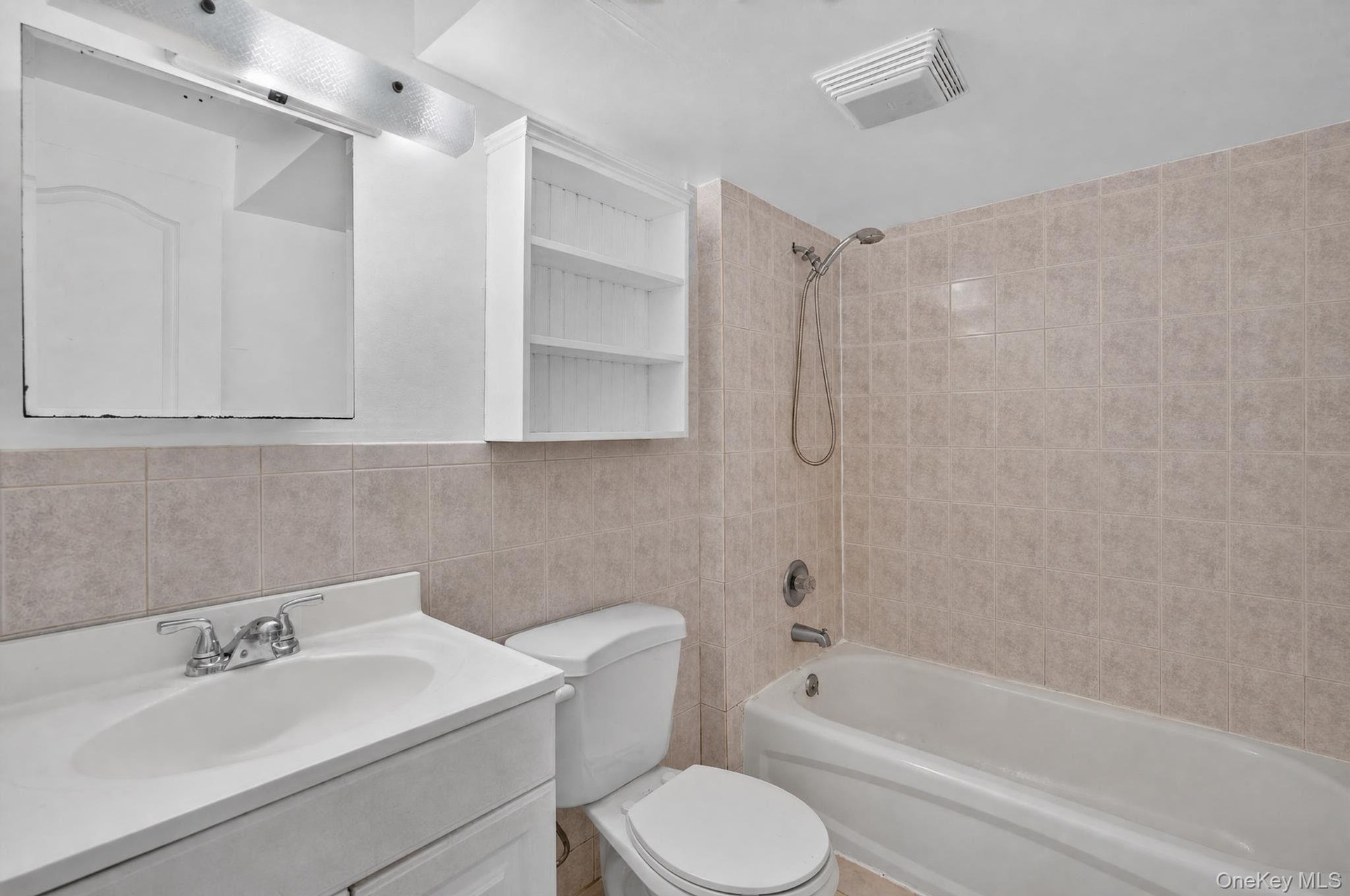 Full bathroom featuring a single vanity, a toilet, a tub with a shower head, and tiled walls