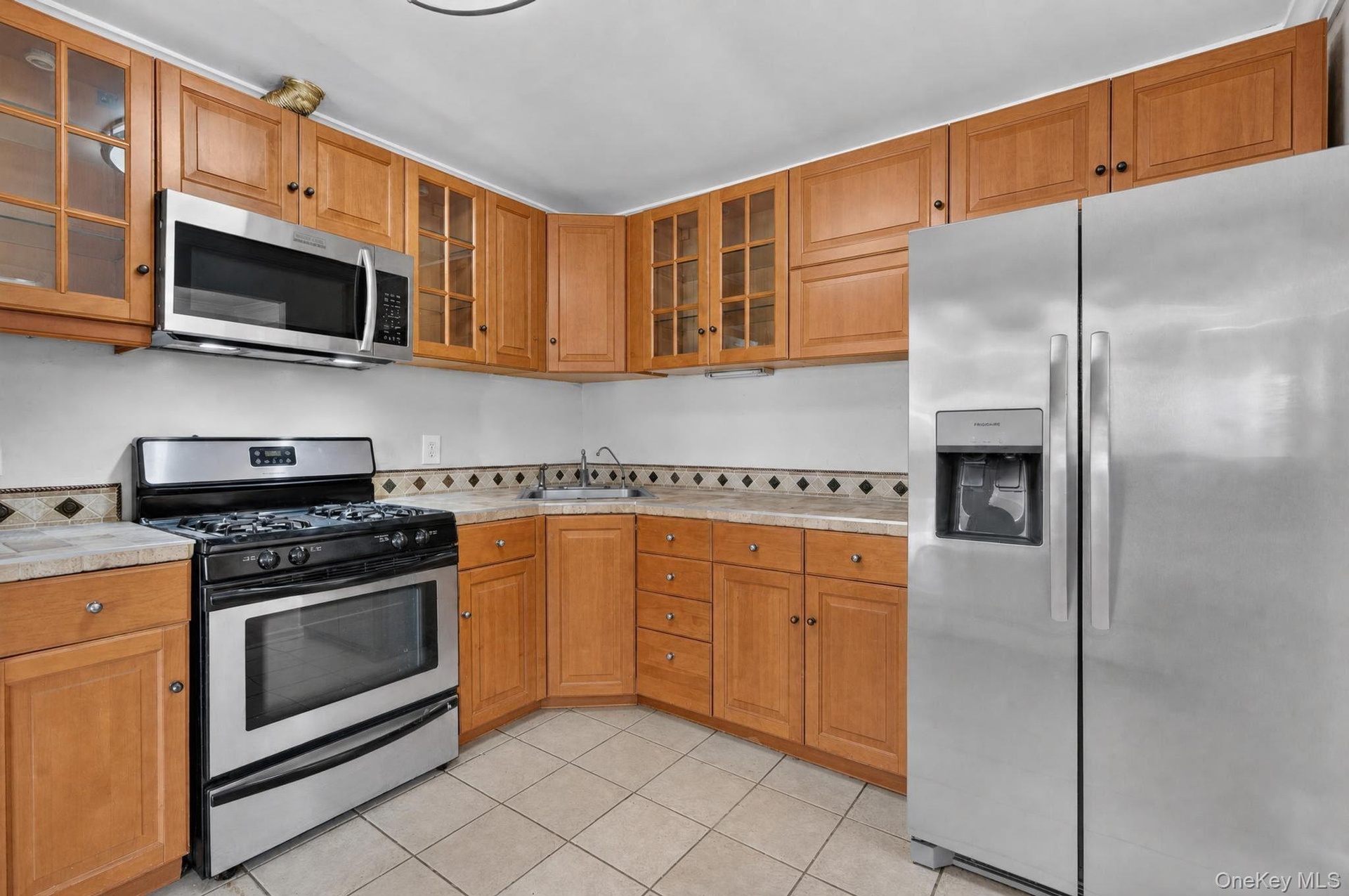 Kitchen featuring stainless steel appliances, light wood cabinetry, and a patterned tile backsplash