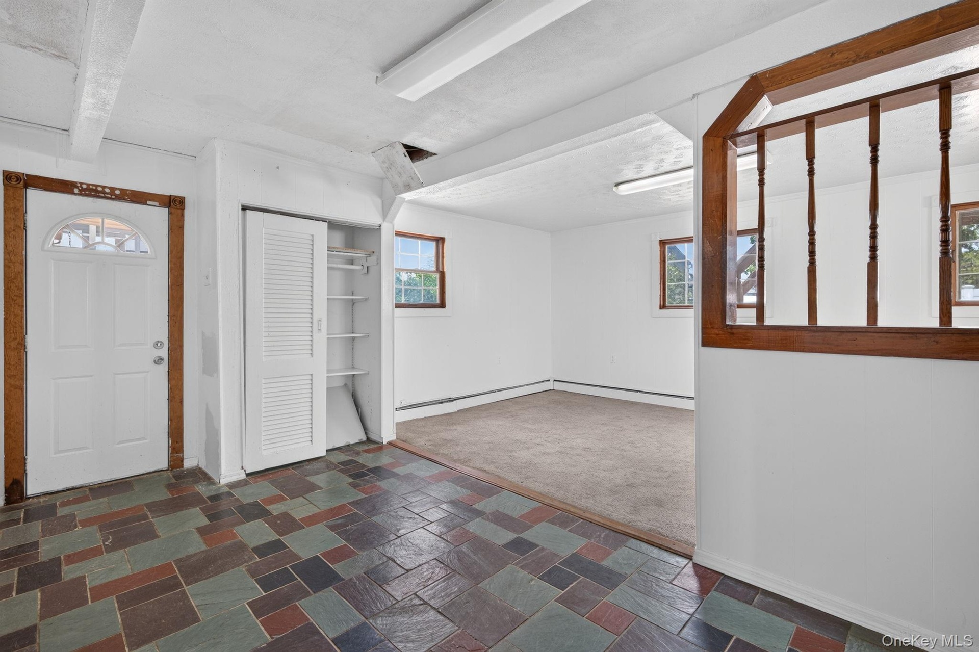 Multi-color slate tile flooring at entry, featuring a white door with an arched window, and a built-in closet with louvered bi-fold doors and shelving