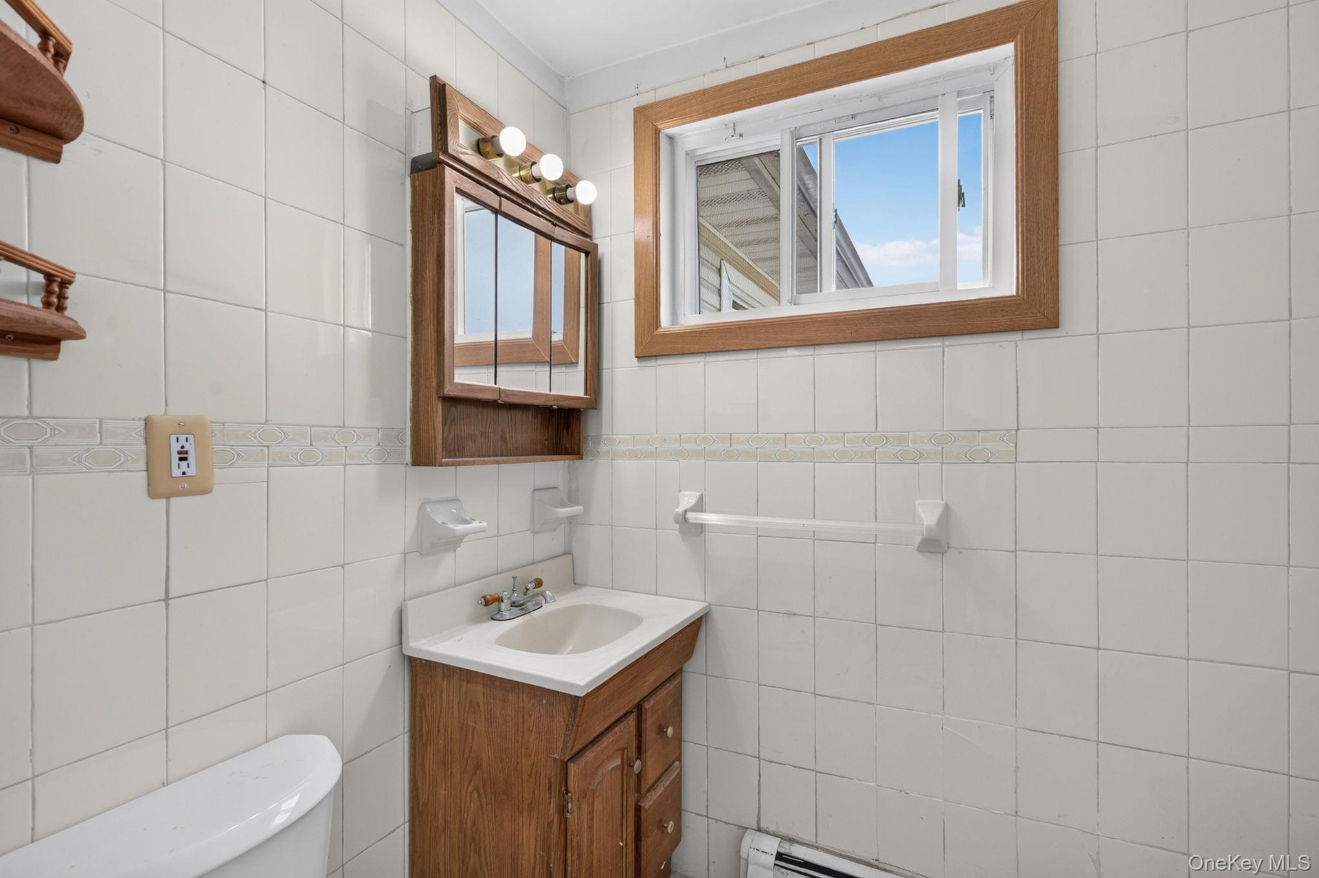 Bathroom featuring white square wall tiles with a decorative border, a wood-finish vanity with an integrated sink, and a matching wood-finish medicine