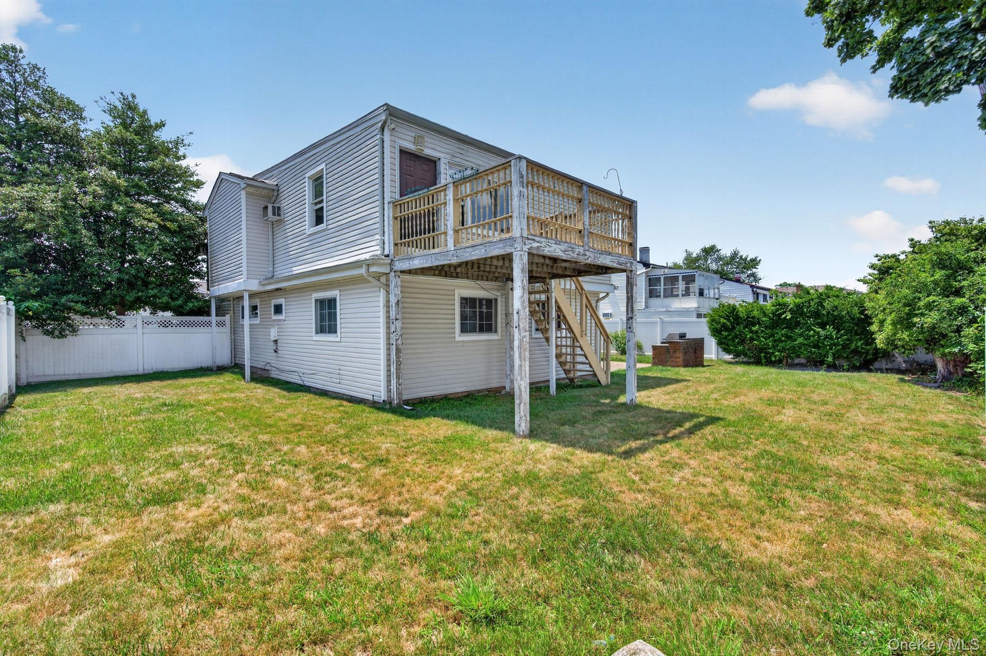 Spacious backyard featuring a multi-level structure with a second-story deck, exterior staircase, and vinyl siding